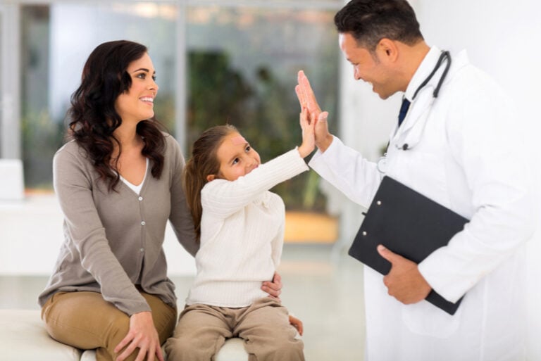 glückliches kleines mädchen und kinderarzt, die nach der ärztlichen untersuchung high five machen