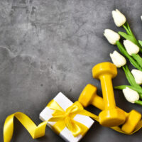 Gelbe Hanteln, Geschenk mit Tulpenstrauß auf grauem Betongrund