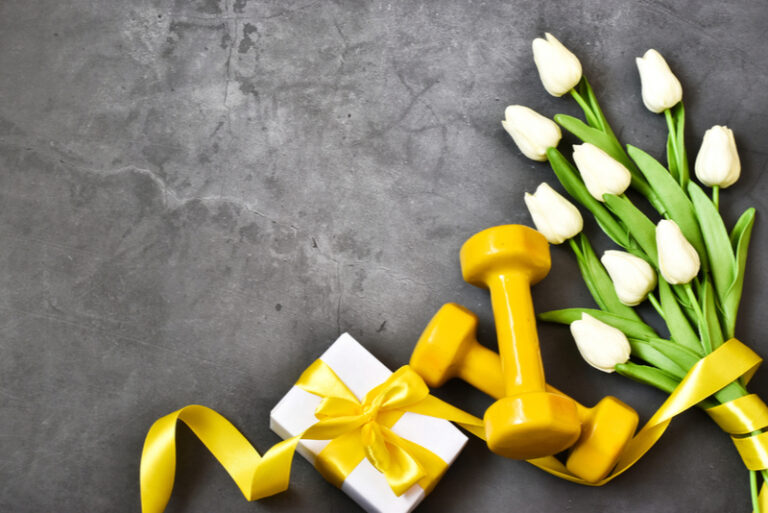 Gelbe Hanteln, Geschenk mit Tulpenstrauß auf grauem Betongrund