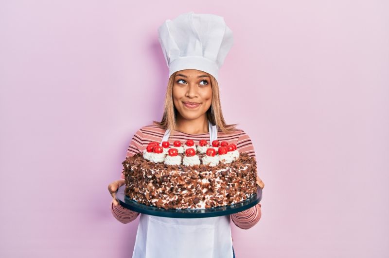 eine Frau in Kochuniform und Hut und eine Geburtstagstorte