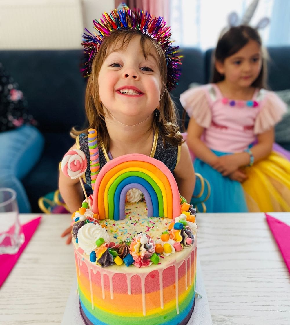 Kleines Mädchen feiert dritten Geburtstag mit einer schönen Regenbogentorte